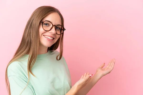 若いリトアニア人女性はピンクを背景に孤立眼鏡をかけ何かを提示 — ストック写真