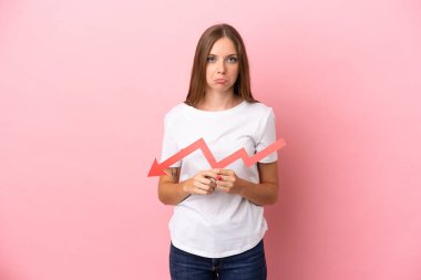 Genç Litvanyalı bir kadın pembe arka planda izole edilmiş, aşağıya doğru ok atıyor ve üzgün bir ifadeyle