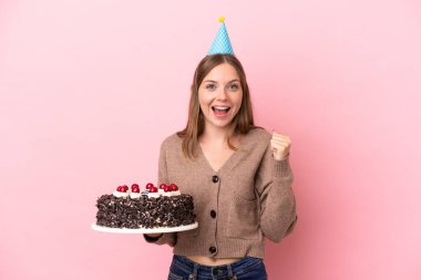 Elinde doğum günü pastası tutan Litvanyalı genç bir kadın pembe arka planda izole bir şekilde zaferi kutluyor.