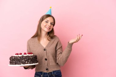 Elinde doğum günü pastası tutan Litvanyalı genç bir kadın. Pembe arka planda izole edilmiş. Gelmesi için ellerini yana uzatıyor.