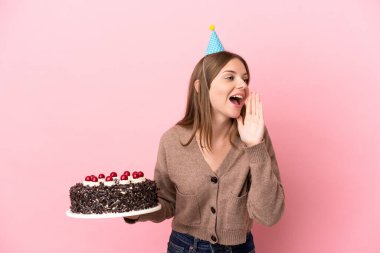 Elinde doğum günü pastası tutan Litvanyalı genç bir kadın pembe arka planda izole bir şekilde ağzı açık bağırıyor.