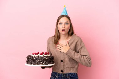 Elinde doğum günü pastası tutan Litvanyalı genç bir kadın pembe arka planda izole edilmiş.