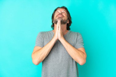 Kıdemli Hollandalı mavi arka planda tek başına avuçlarını bir arada tutuyor. İnsan bir şey ister.