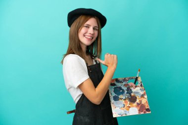 Mavi arka planda kendini beğenmiş ve gururlu bir palet tutan genç bir İngiliz kadın.