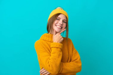 Kışlık ceket giyen genç İngiliz kadın mavi arka planda izole edilmiş gülümsüyor.