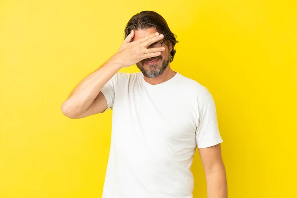 手で目を覆い笑顔で黄色の背景に隔離されたシニアオランダ人男性 — ストック写真