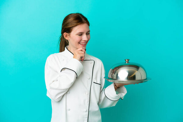 Young chef woman with tray isolated on blue background looking to the side and smiling