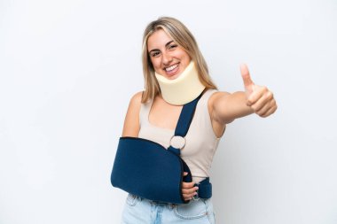 Kırık kollu ve askı takan bir kadın beyaz arka planda izole edilmiş bir şekilde baş parmak hareketi yapıyor.