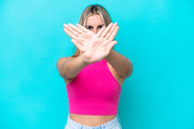 Kafkasyalı genç bir kadın, mavi arka planda izole edilmiş bir şekilde bir eylemi durdurmak için el hareketi yapıyor.