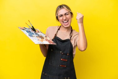 Sarı arka planda izole edilmiş palet tutan beyaz bir kadın zaferi kutluyor.