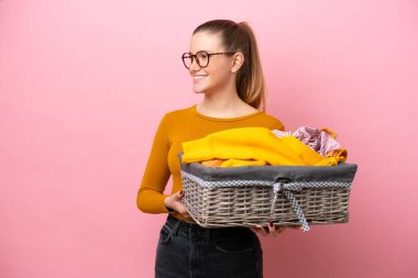 Pembe arka planda izole edilmiş çamaşır sepeti tutan beyaz bir kadın.