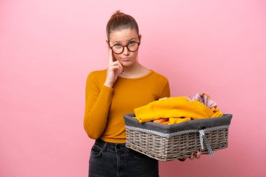 Kafkasyalı genç bir kadın pembe arka planda izole edilmiş çamaşır sepetini tutarken bir fikir düşünüyor.