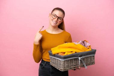 Pembe arka planda izole edilmiş çamaşır sepetini tutan beyaz bir kadın baş parmak işareti yapıyor.