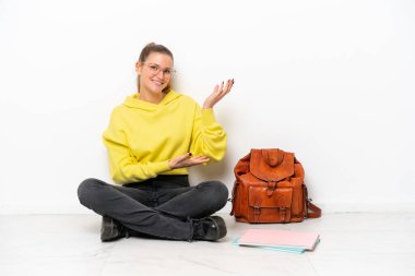 Beyaz arka planda beyaz bir zeminde oturan beyaz tenli genç bir kadın davet edilmek için ellerini yana uzatıyor.