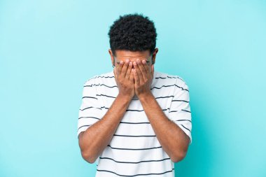 Genç Brezilyalı adam mavi arka planda izole edilmiş, yorgun ve hasta bir ifadeyle.