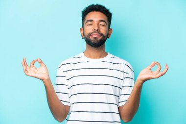 Zen pozisyonunda mavi arka planda izole edilmiş genç Brezilyalı adam.