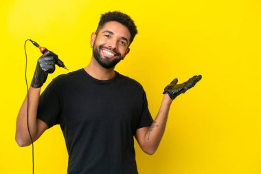 Tattoo artist man Brazilian man isolated on yellow background extending hands to the side for inviting to come