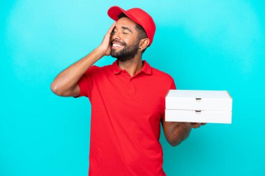 İş üniformalı Brezilyalı bir adam mavi arka planda izole edilmiş pizza kutularını topluyor.