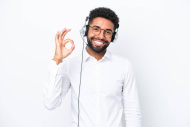 Tele pazarlamacı Brezilyalı adam beyaz arka planda izole edilmiş bir kulaklıkla çalışıyor. Parmaklarıyla tamam işareti gösteriyor.