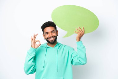Beyaz arka planda izole edilmiş genç Brezilyalı bir adam elinde boş bir konuşma balonu tutuyor ve tamam işareti yapıyor.