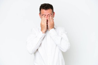 Beyaz arka planda izole edilmiş beyaz tenli yakışıklı adam gözlerini elleriyle kapatıyor.