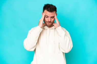 Kafkasyalı yakışıklı genç adam mavi arka planda başağrısı ile izole edilmiş.