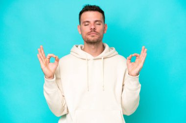 Beyaz tenli yakışıklı adam, mavi arka planda Zen pozuyla izole edilmiş.