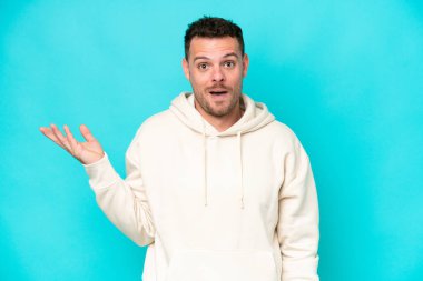 Mavi arka planda izole edilmiş beyaz, yakışıklı genç bir adam şüpheli hareketlerde bulunuyor.