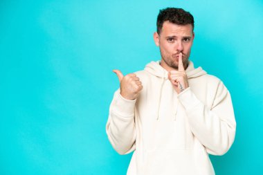 Mavi arka planda izole edilmiş beyaz, yakışıklı genç bir adam. Yan tarafı işaret ediyor ve sessiz hareketler yapıyor.