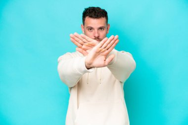 Beyaz tenli yakışıklı bir adam mavi arka planda izole edilmiş bir şekilde bir hareketi durdurmak için el hareketi yapıyor.