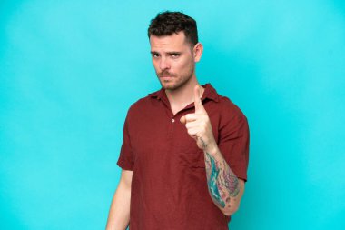 Kafkasyalı yakışıklı adam mavi arka planda izole edilmiş hayal kırıklığına uğramış ve ön tarafı işaret ediyor.
