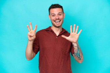 Beyaz tenli yakışıklı adam mavi arka planda izole edilmiş, parmaklarıyla sekizi sayıyor.