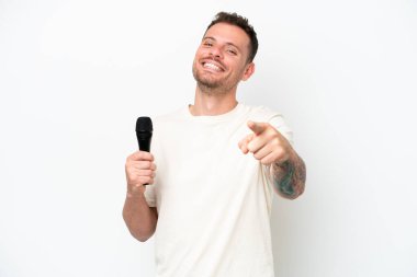 Young caucasian singer man picking up a microphone isolated on white background pointing front with happy expression