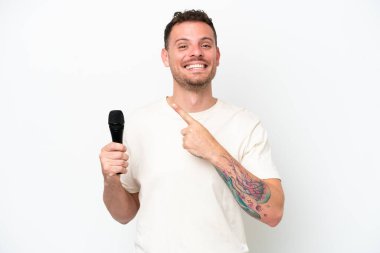 Young caucasian singer man picking up a microphone isolated on white background pointing to the side to present a product
