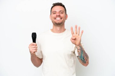 Young caucasian singer man picking up a microphone isolated on white background happy and counting four with fingers