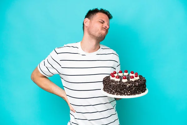 Young caucasian man holding birthday cake isolated on blue background suffering from backache for having made an effort