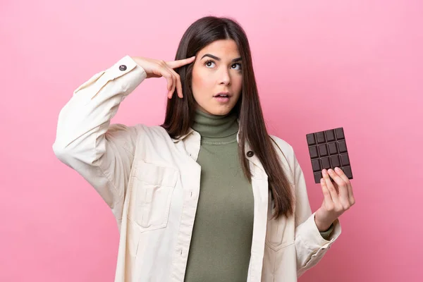 Young Brazilian woman with chocolat isolated on pink background having doubts and thinking