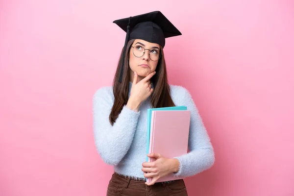 若いです学生ブラジル人女性身に着けています卒業帽子孤立ピンクの背景に疑問を持って — ストック写真