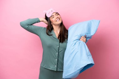 Genç Brezilyalı bir kadın pembe arka planda izole edilmiş pijamalarıyla ve elinde bir yastıkla esniyor.