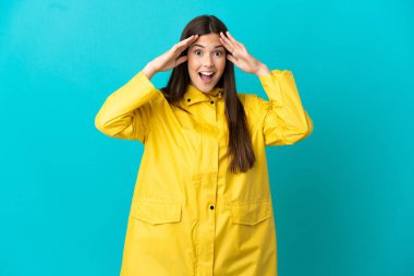 Teenager Brazilian girl wearing a rainproof coat over isolated blue background with surprise expression