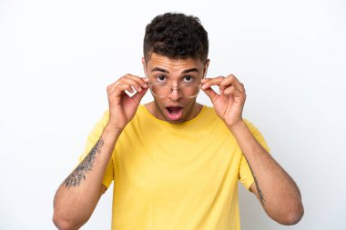 Genç Brezilyalı adam beyaz arka planda gözlüklü ve şaşırmış bir ifadeyle izole edilmiş.