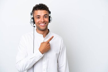 Tele pazarlamacı Brezilyalı beyaz arka planda izole edilmiş bir kulaklıkla çalışan bir adam bir ürün sunmak için kenarı işaret ediyor