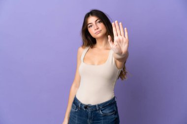 Mor arka planda izole edilmiş genç beyaz kadın dur hareketi yapıyor.