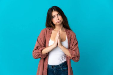 Mavi arka planda izole edilmiş genç beyaz kadın avuç içlerini bir arada tutuyor. İnsan bir şey ister.