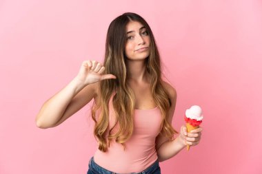 Kornet dondurması olan beyaz bir kadın pembe arka planda izole edilmiş ve olumsuz bir ifadeyle baş parmağını gösteriyor.