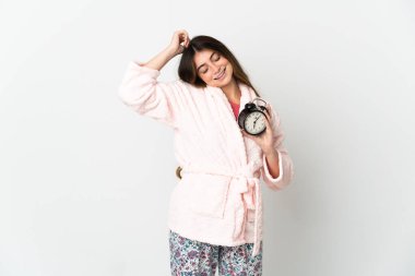 Young caucasian woman isolated on white background in pajamas and holding clock doing victory gesture