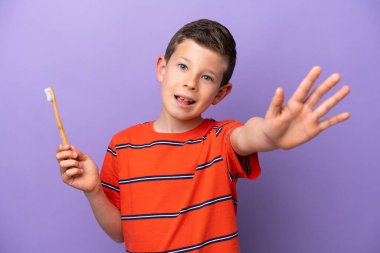 Little boy brushing teeth isolated on purple background saluting with hand with happy expression