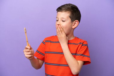 Mor arka planda diş fırçalayan küçük çocuk şaşırmış ve şok olmuş bir yüz ifadesiyle.