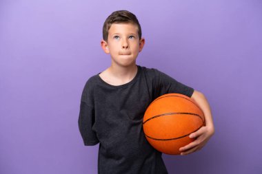 Mor arka planda basketbol oynayan küçük çocuk yukarı bakıyor.