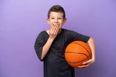Little boy playing basketball isolated on purple background happy and smiling covering mouth with hand